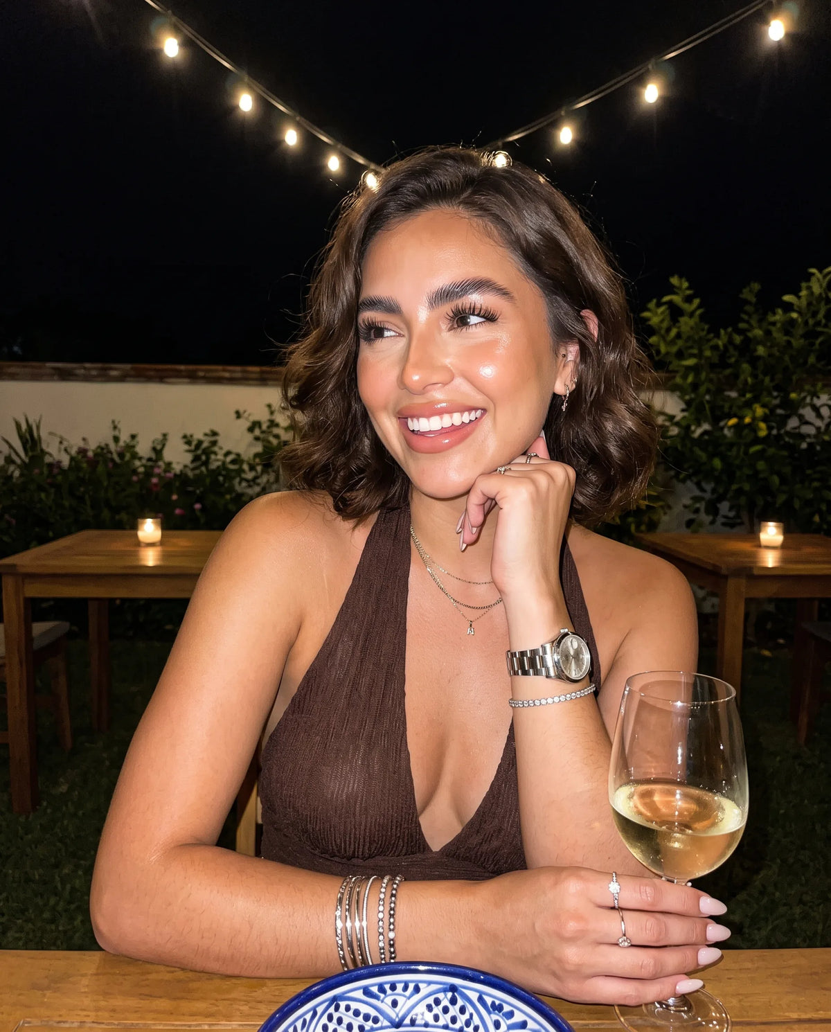 Mujer sonriendo en una cena al aire libre bajo luces colgantes — perfumes para mujer para una cita